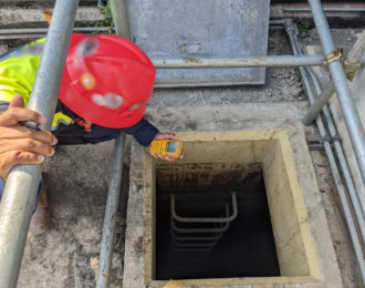 Worker and safety officer take data for gas test before confine space activity.